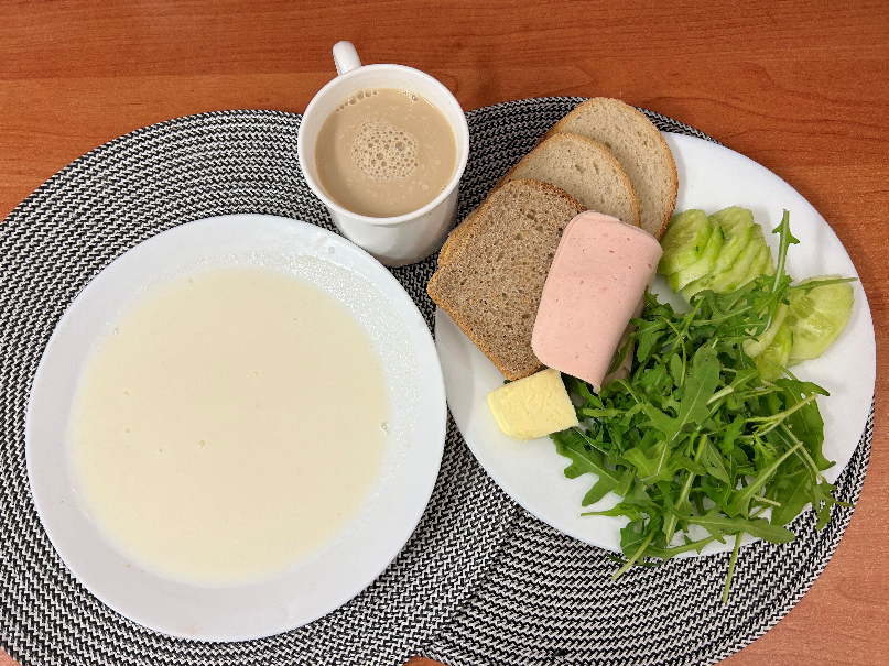 Na zdjęciu znajduje się: Kasza manna na mleku, Kawa zbożowa z mlekiem, Chleb mieszany pszenno - żytni, Chleb Graham, Masło extra 82%, Filet zapiekany drobiowy, Ogórek świeży, Rukola